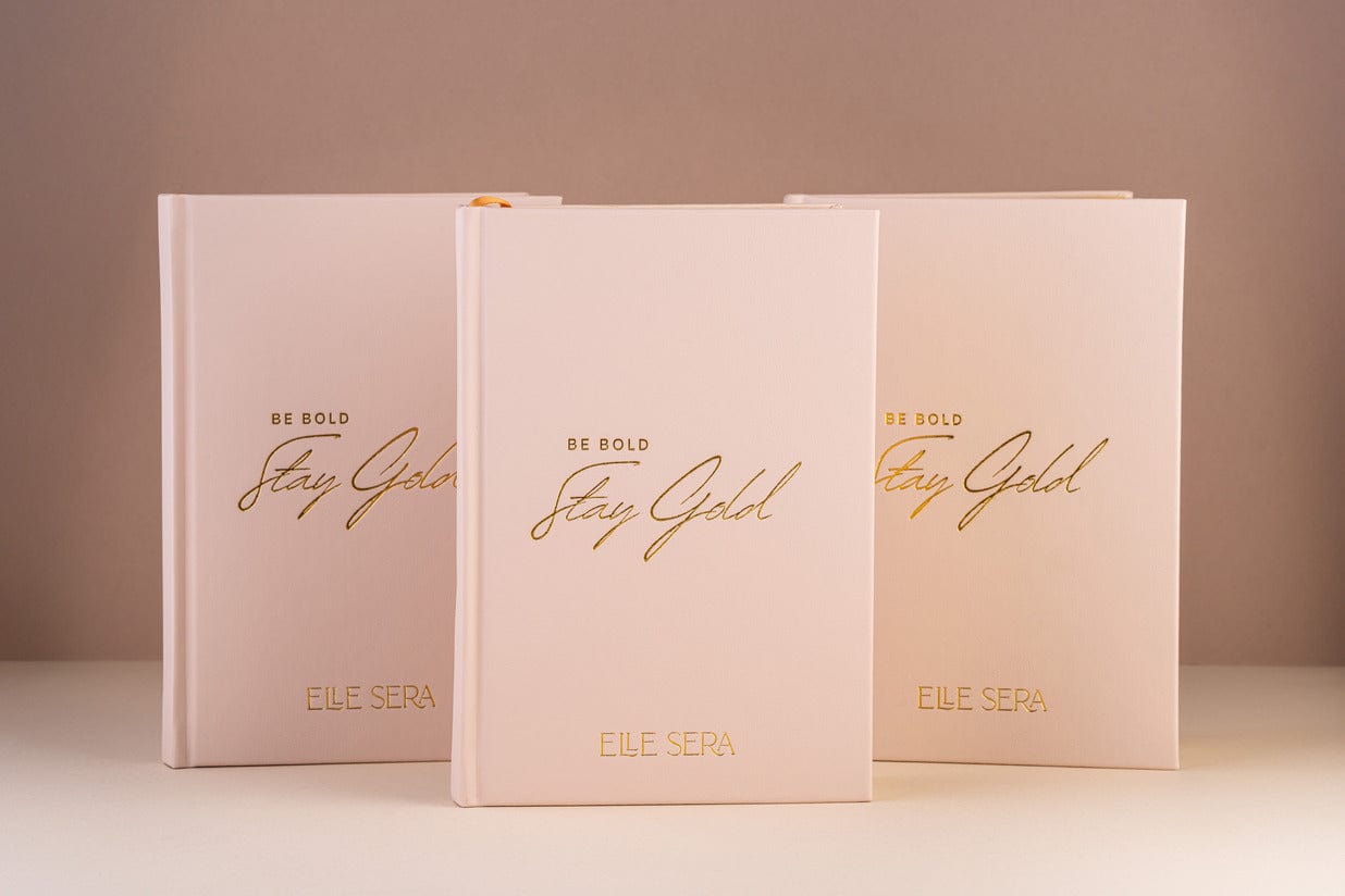 Three-Month Wellness Journal - Growth & Habits | Daily Clarity in blush pink hardcover with gold embossed text 'Be Bold Stay Gold' by Elle Sera. Ideal for tracking wellness, habits, and mindfulness.