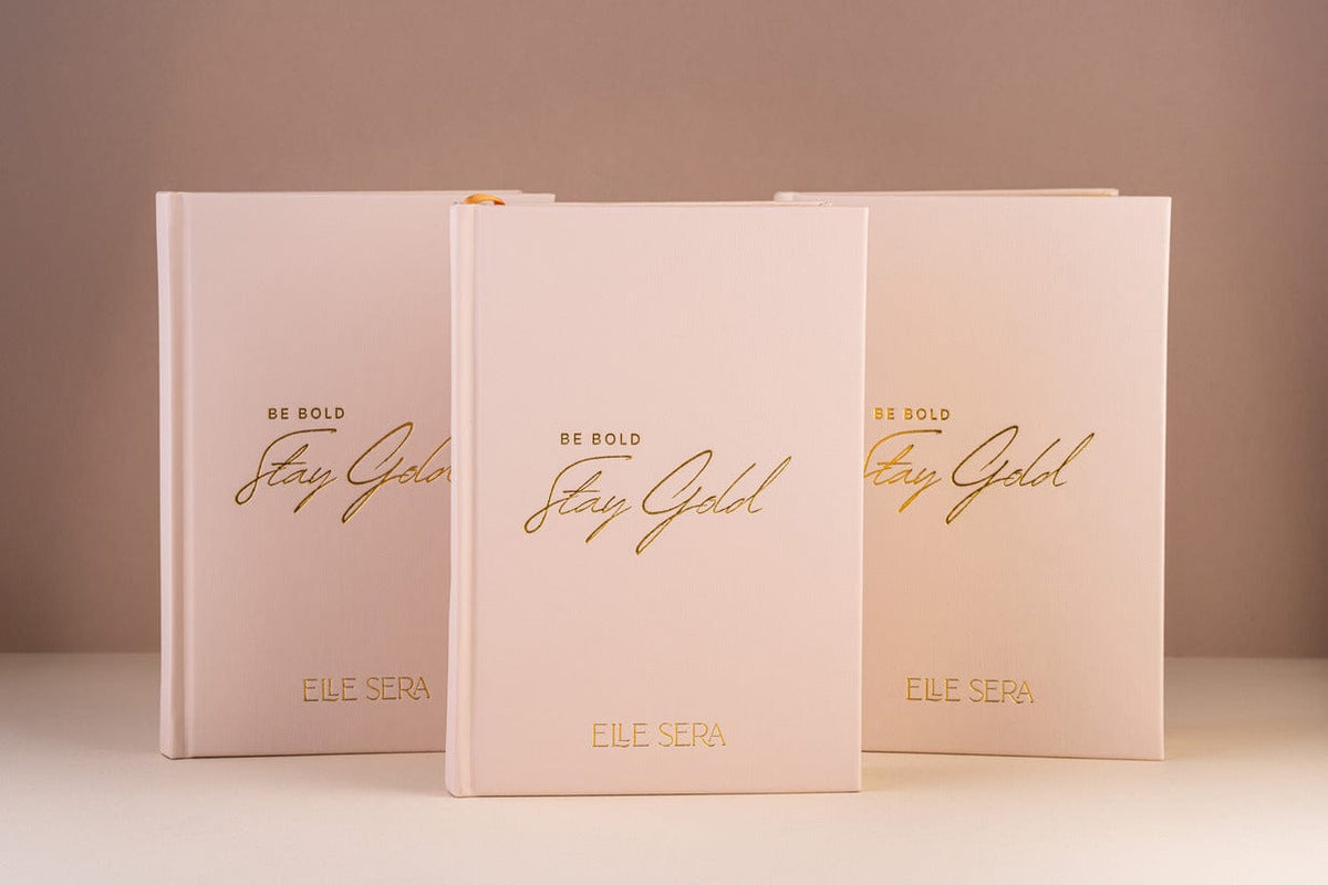 Three-Month Wellness Journal - Growth & Habits | Daily Clarity in blush pink hardcover with gold embossed text 'Be Bold Stay Gold' by Elle Sera. Ideal for tracking wellness, habits, and mindfulness.