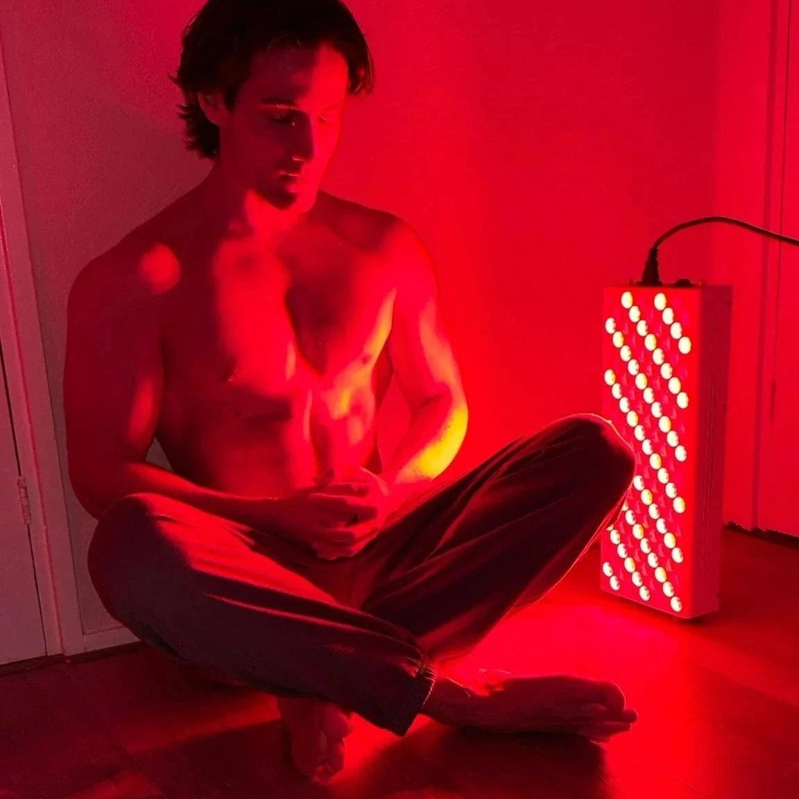 Man meditating in front of Red Light Elite Series 506 therapy device for deep tissue healing and relaxation. Enhances recovery and reduces pain.