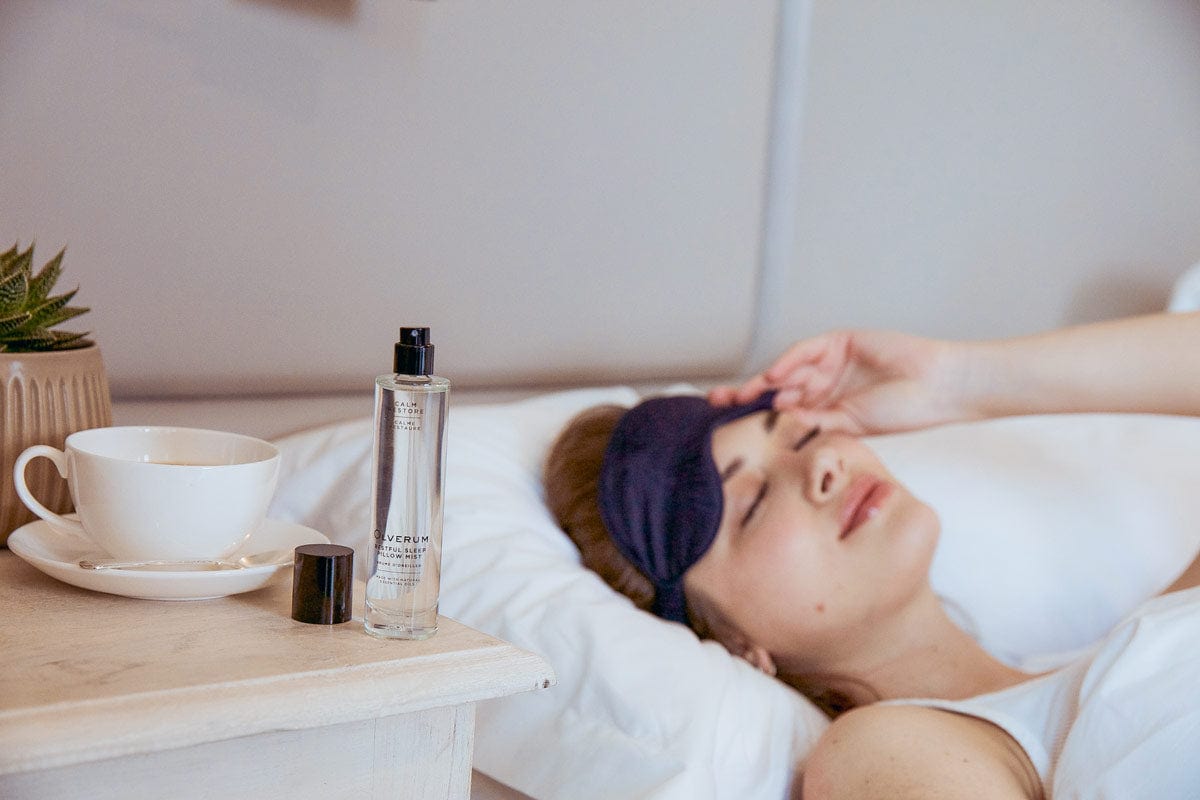 Woman relaxing in bed with Olverum Restful Sleep Pillow Mist on bedside table, part of a calming bedtime routine.