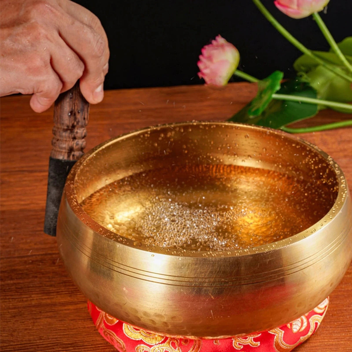 Handmade antique singing bowl with wooden mallet on red cushion, set in a forest stream for meditation and spiritual clarity.
