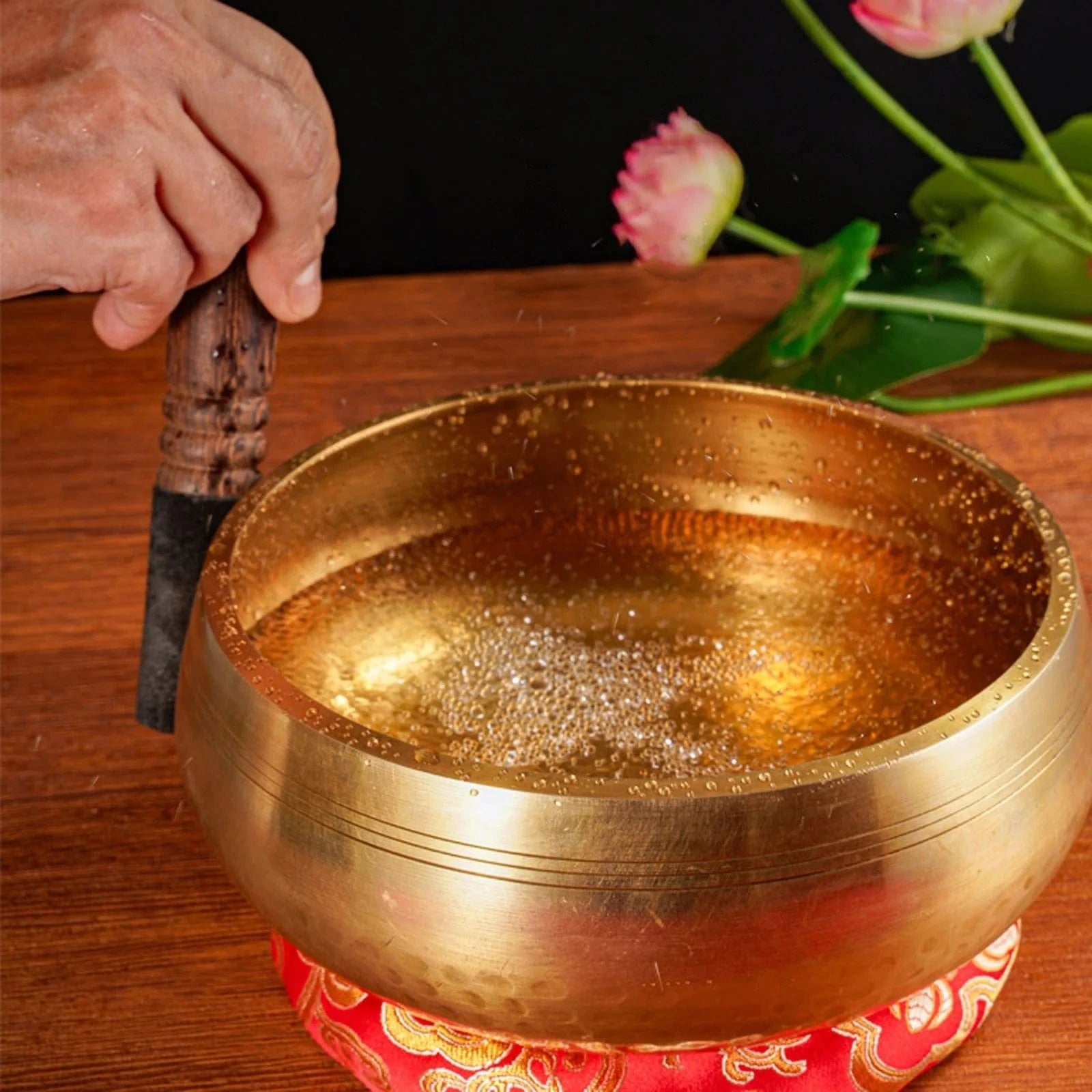 Handmade antique singing bowl with wooden mallet on red cushion, set in a forest stream for meditation and spiritual clarity.
