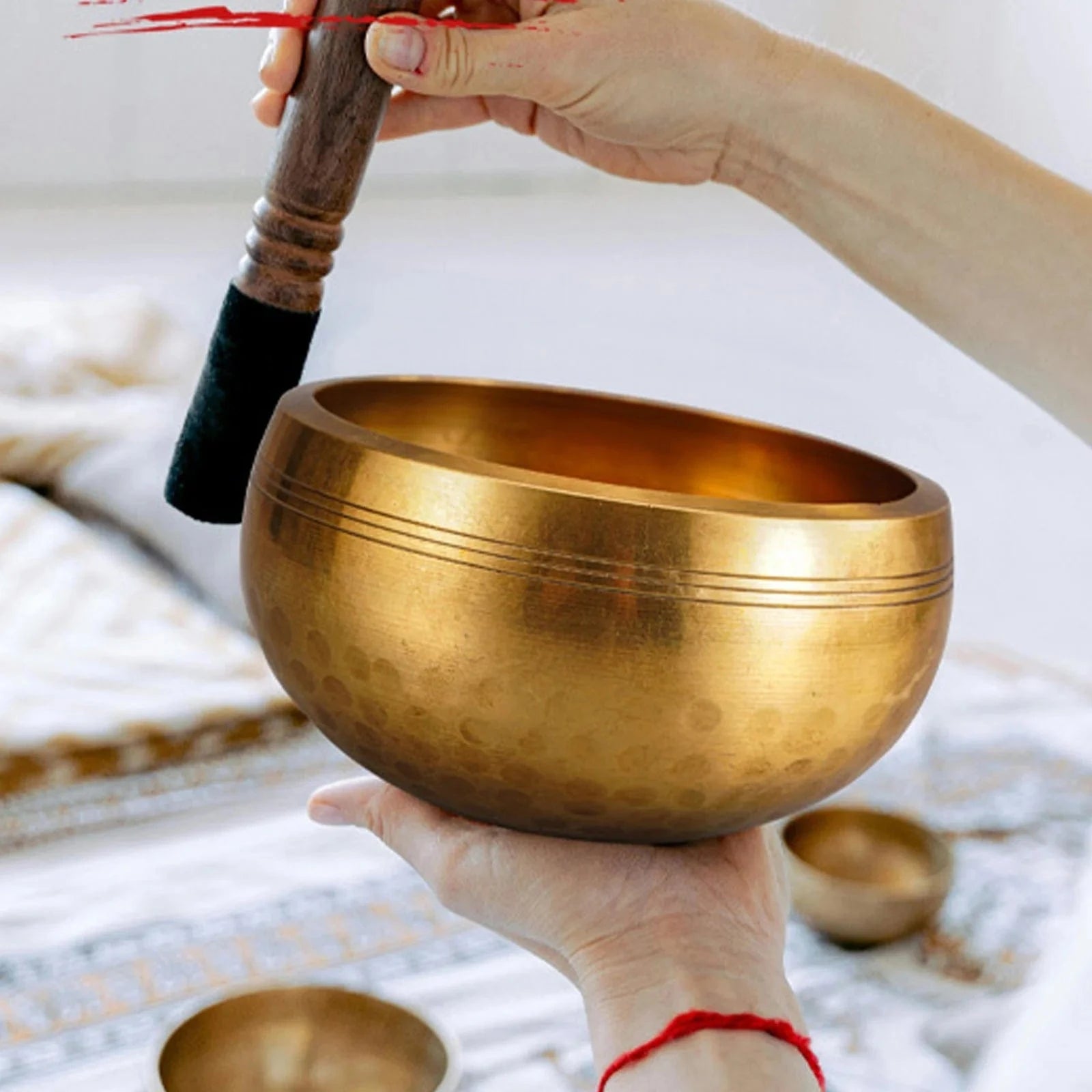 Handmade antique singing bowl with wooden mallet on red cushion, set in a forest stream for meditation and spiritual clarity.