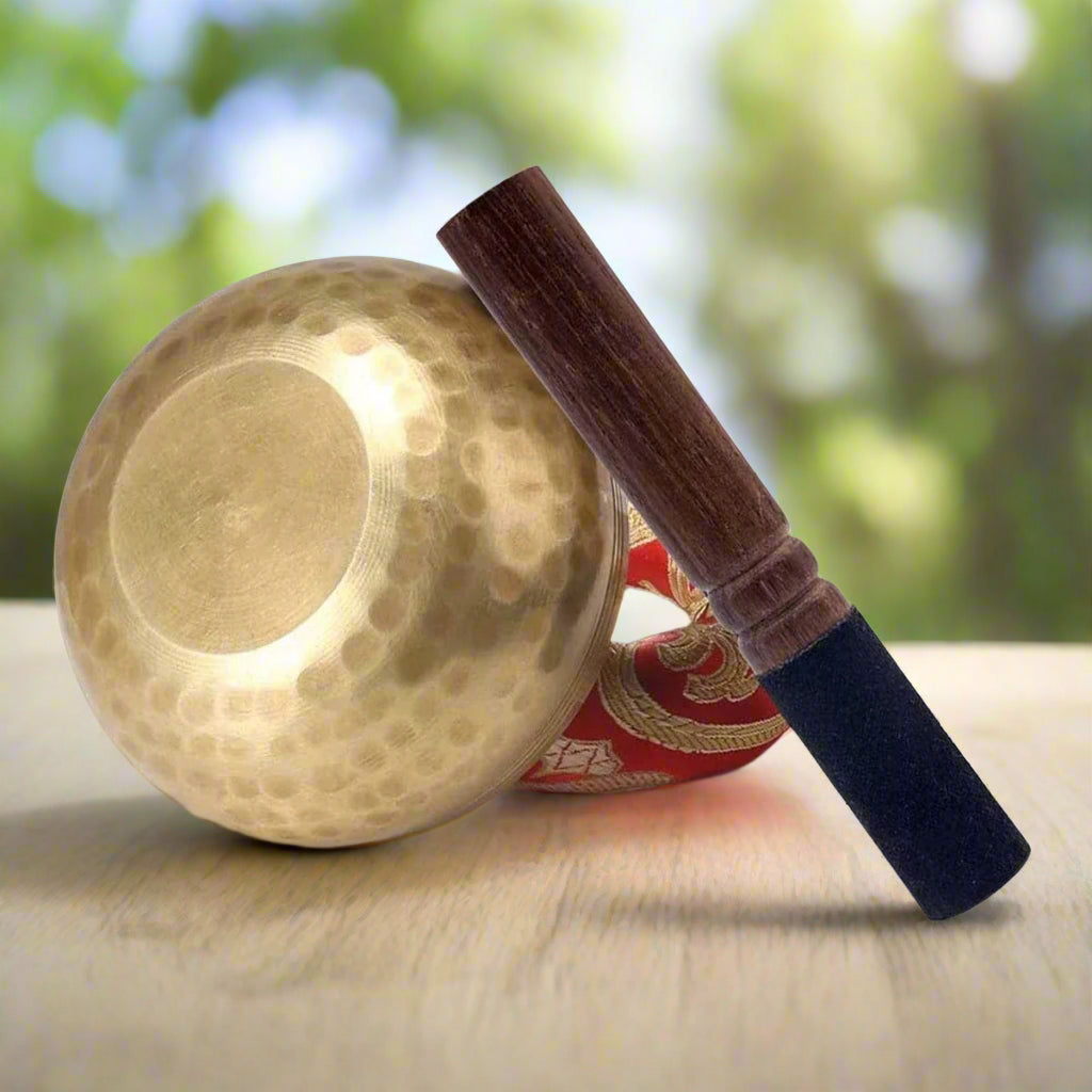 Handmade antique singing bowl with wooden mallet on red cushion, set in a forest stream for meditation and spiritual clarity.